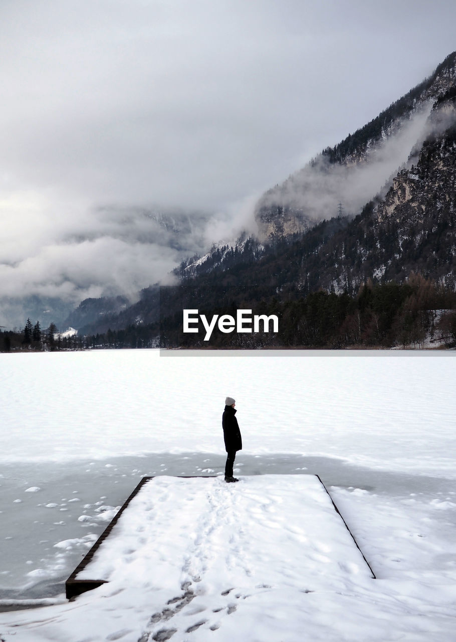 Side view of woman standing on frozen lake against mountain