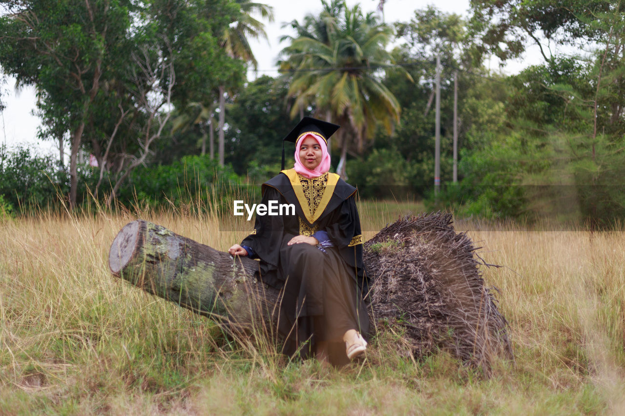 Woman in graduation gown sitting on log