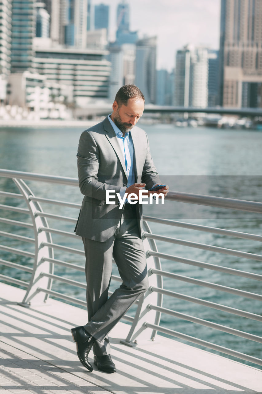 Young businessman with a phone in his hands, standing in a big city among high-rise buildings.