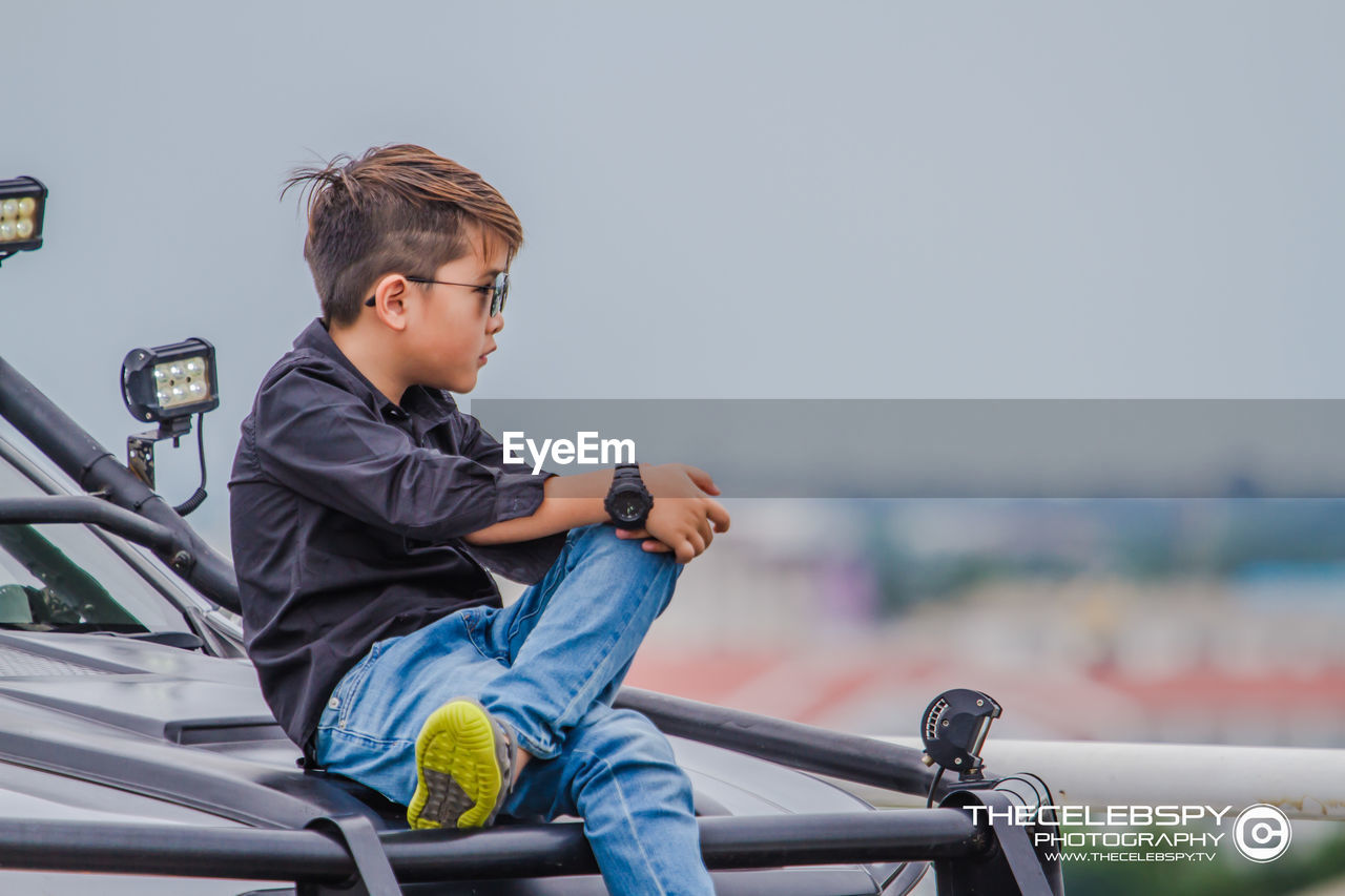 SIDE VIEW OF BOY SITTING ON VEHICLE