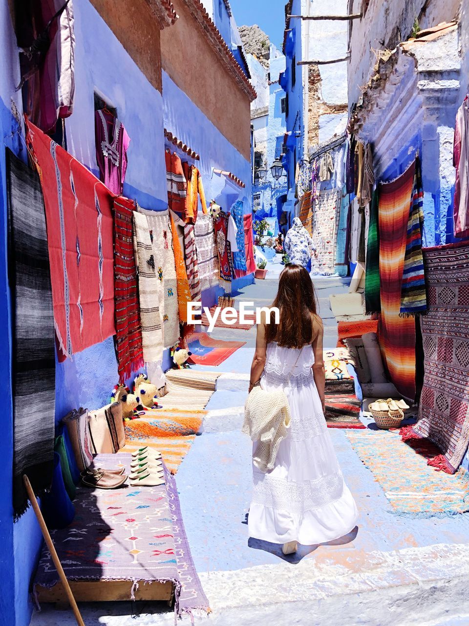 Rear view of woman walking amidst colorful shawls at alley in city
