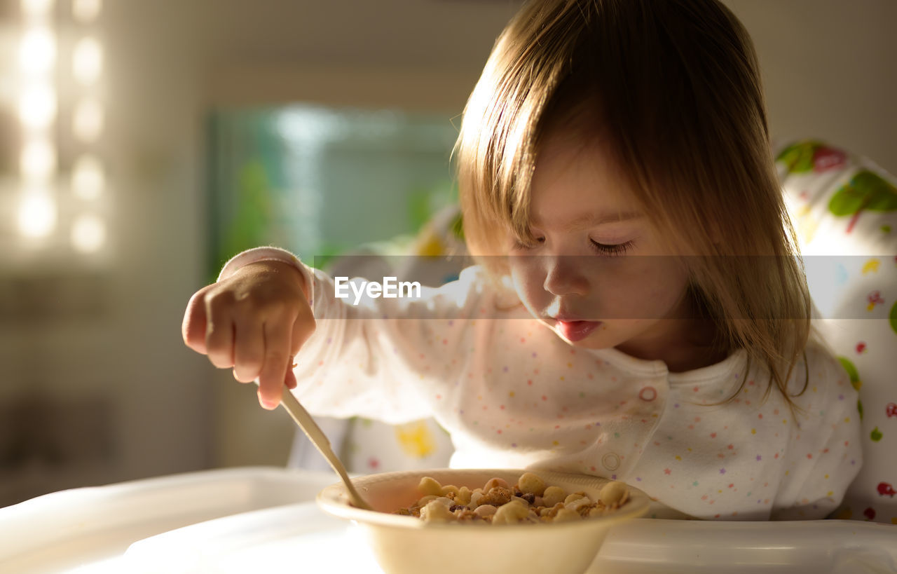 Two years old eats porridge by herself with a spoon. child development concept