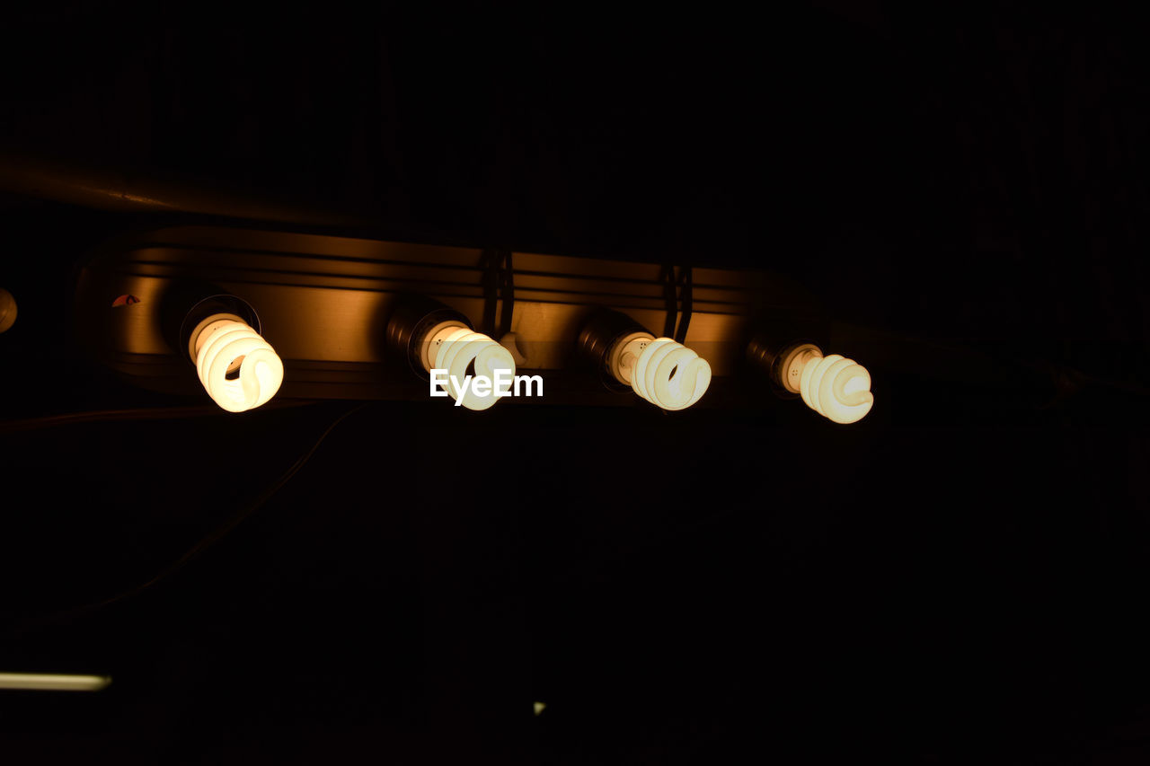 Low angle view of illuminated energy efficient lightbulbs against black background