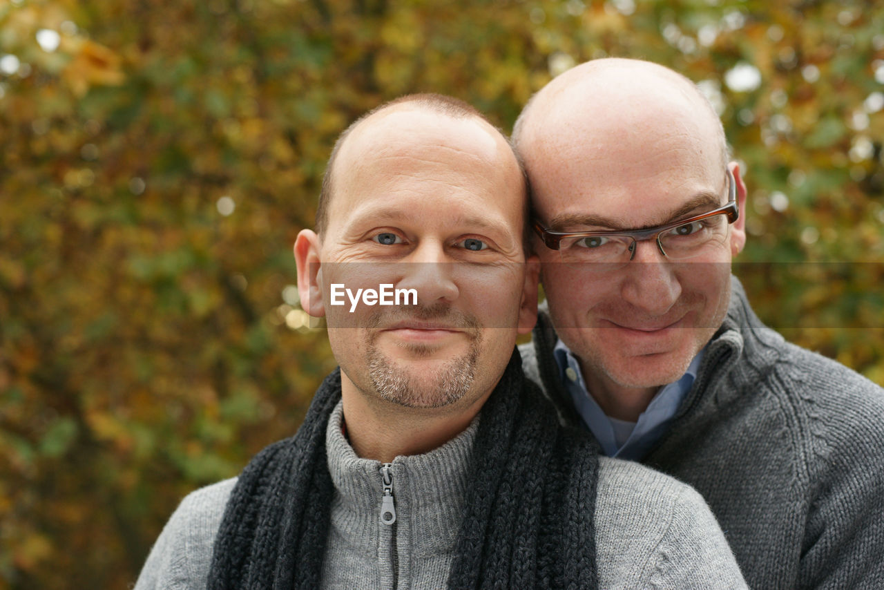 Portrait of smiling gay couple against trees in park