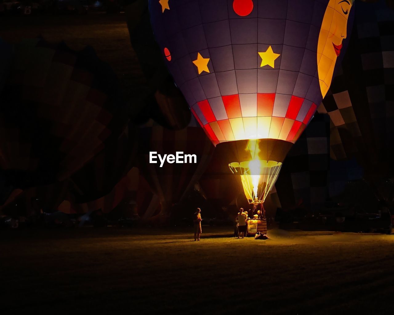 People around lit hot air balloon at night