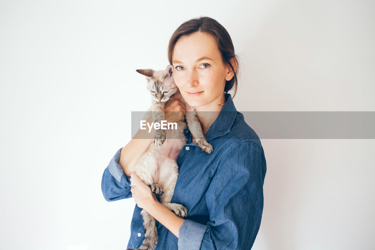 Portrait of woman holding cat against white background