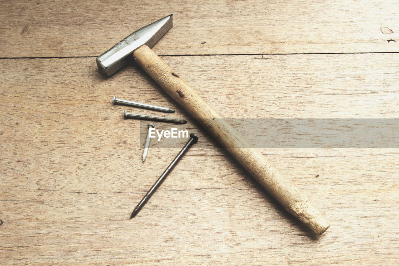 High angle view of hammer with nails on wooden table