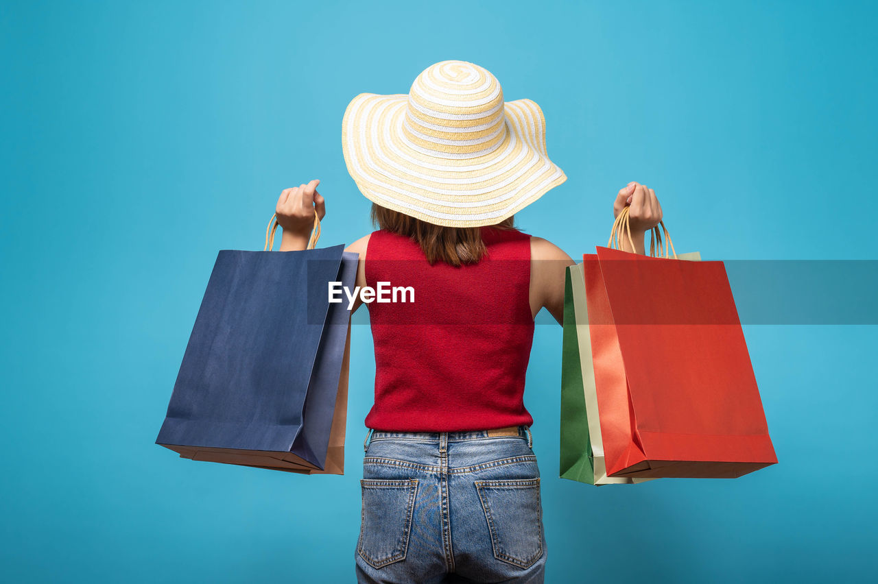 Rear view of woman with shopping bags standing against blue background