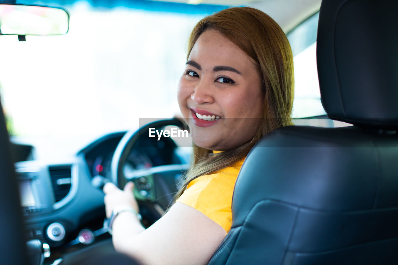 PORTRAIT OF A SMILING YOUNG WOMAN SITTING IN CAR