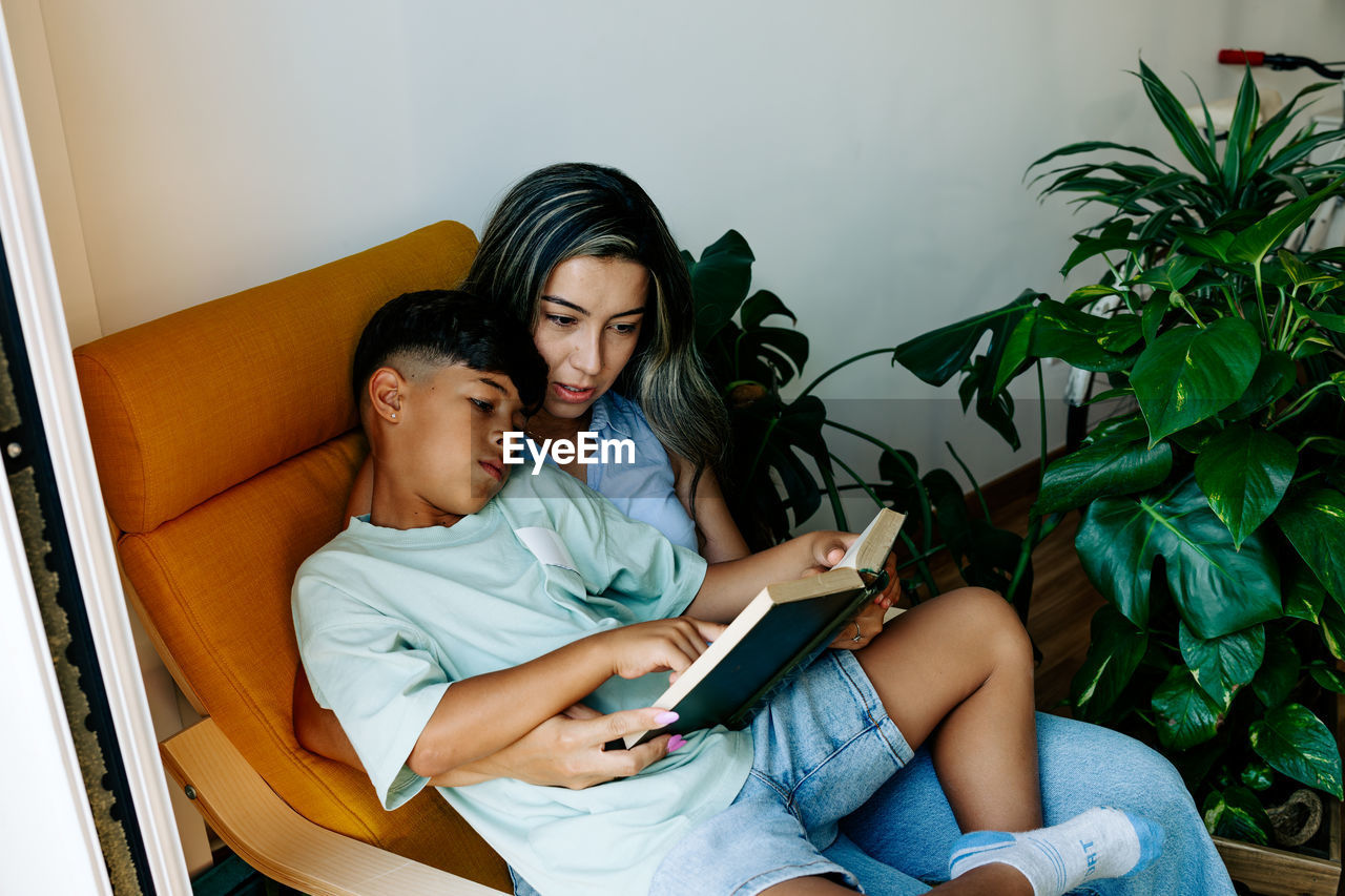 Young family mother and son reading a book in sofa at home