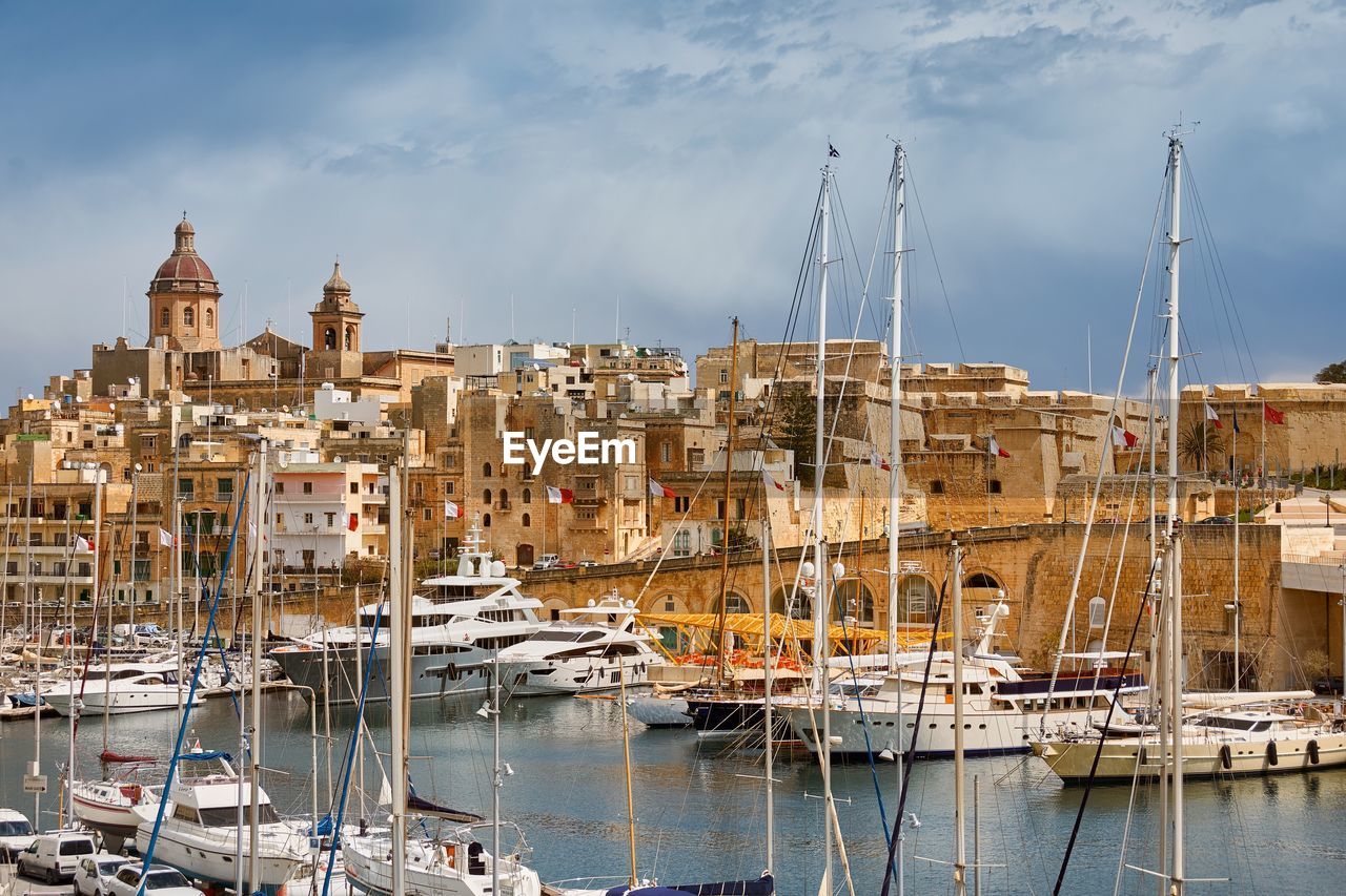 Sailboats moored on harbor by buildings against sky