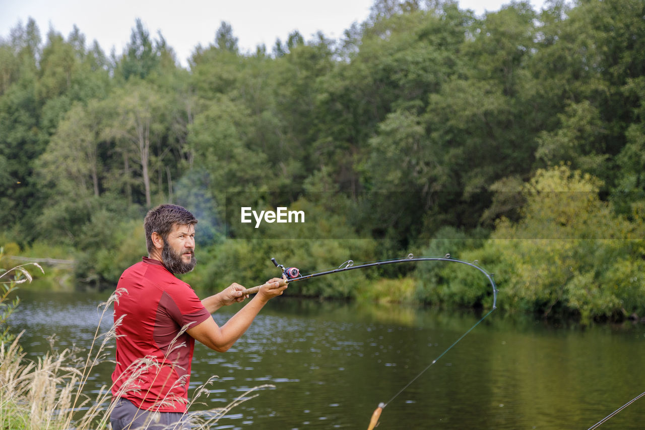 A man with a beard is fishing on the river, casting a line.