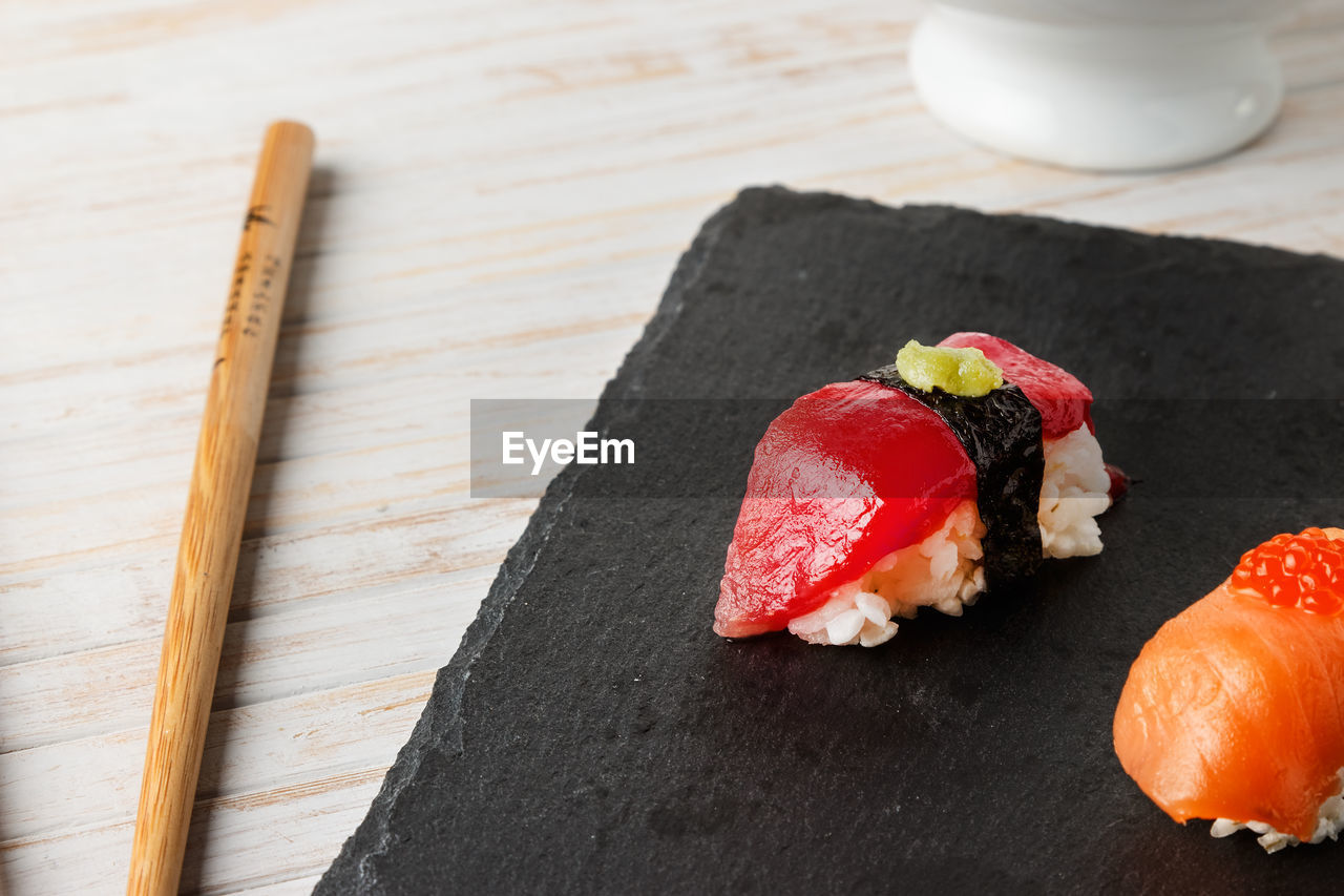 Red tuna nigiri with nori seaweed and wasabi paste on black slate stone with chopsticks. raw fish.