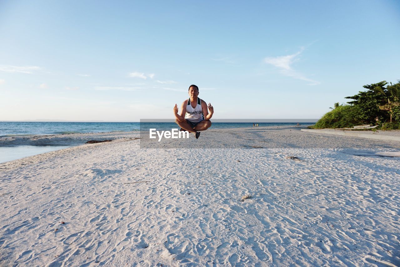 Man meditating on beach against sky