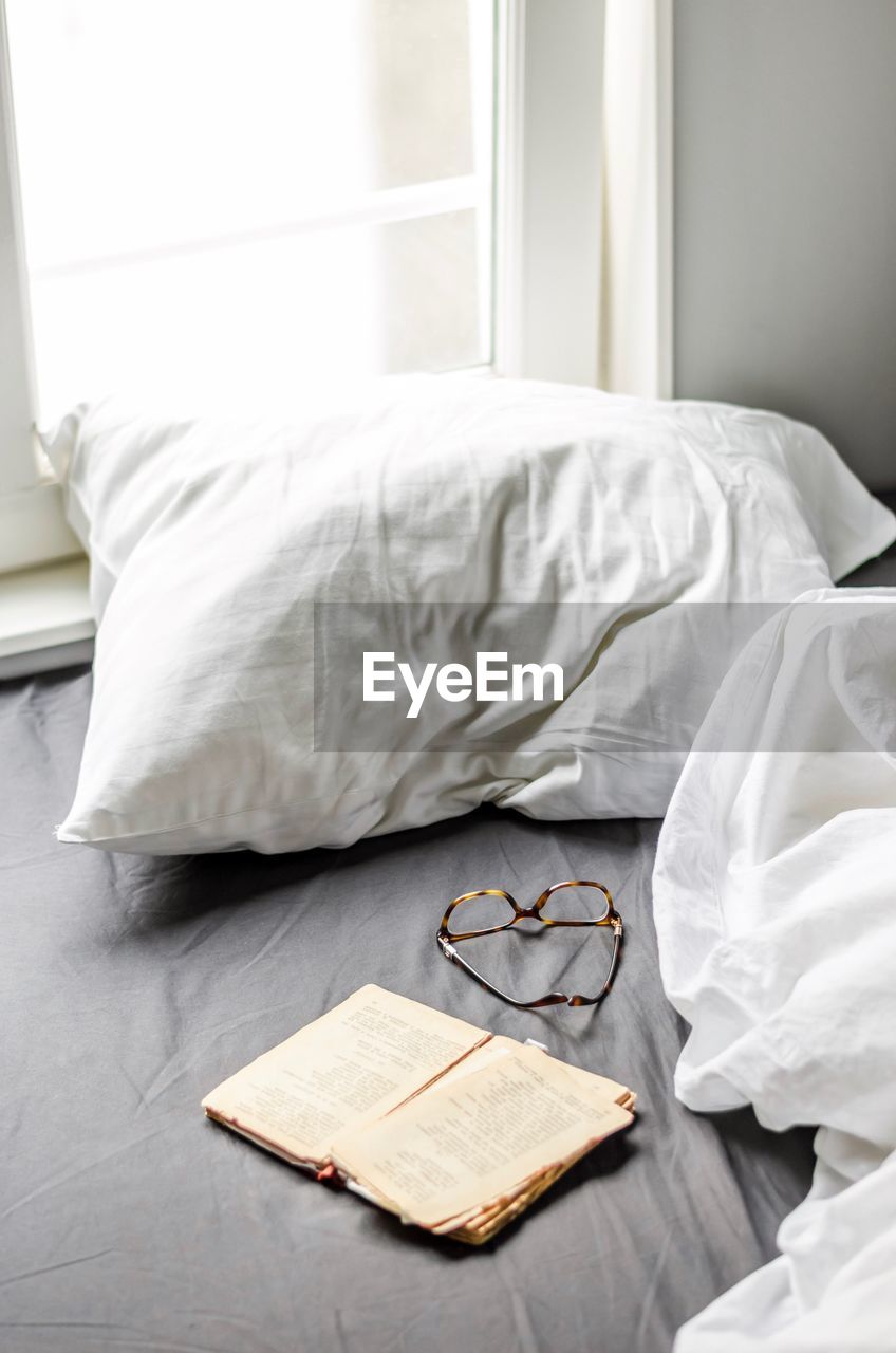 Open book with eyeglasses on bed at home