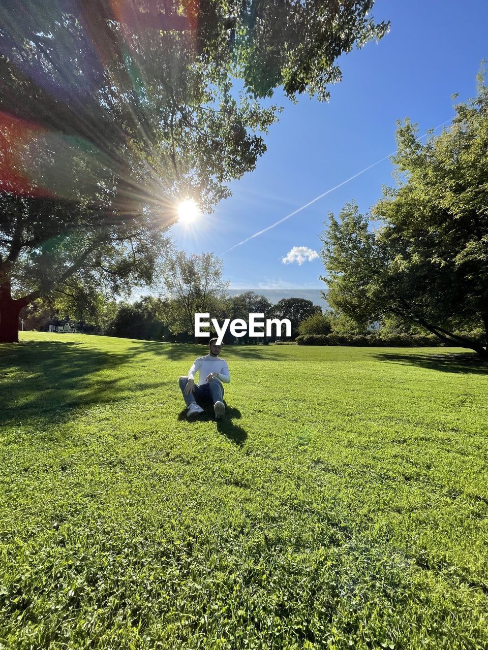 MAN SITTING ON FIELD AGAINST BRIGHT SUN