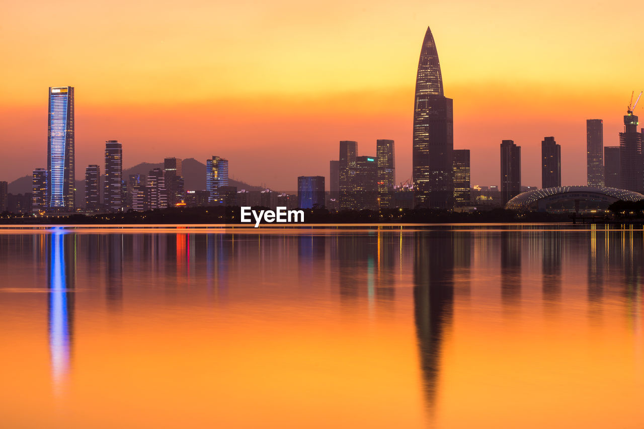 Reflection of illuminated buildings in lake against orange sky