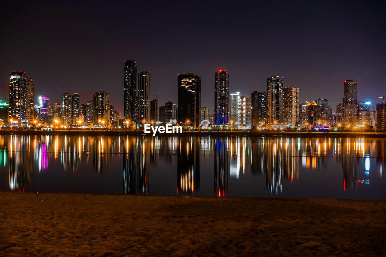 Illuminated buildings by river against sky at night