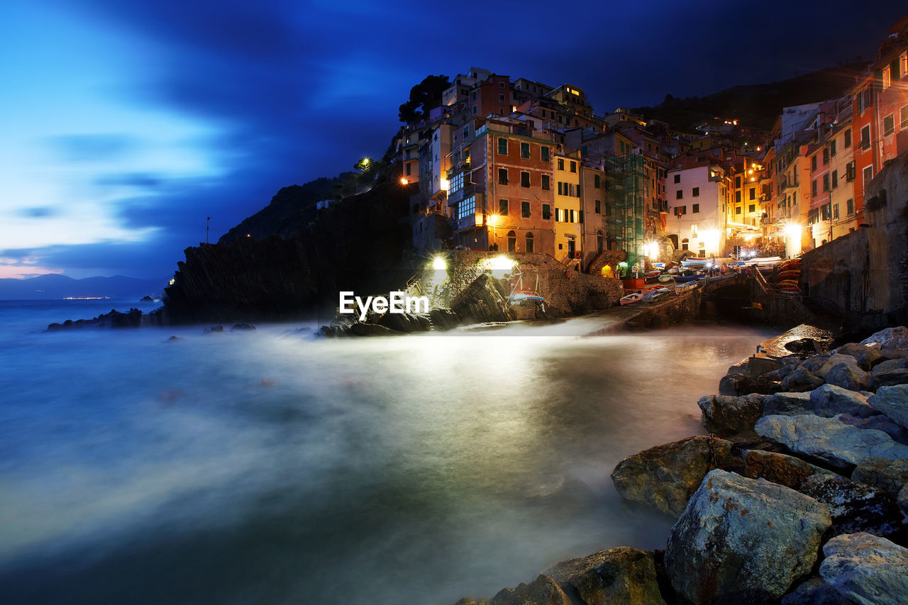 Illuminated building at houses in manarola by sea at dusk