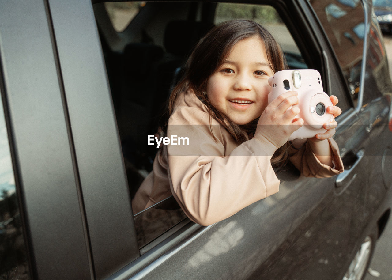 Portrait of young girl in car holding camera