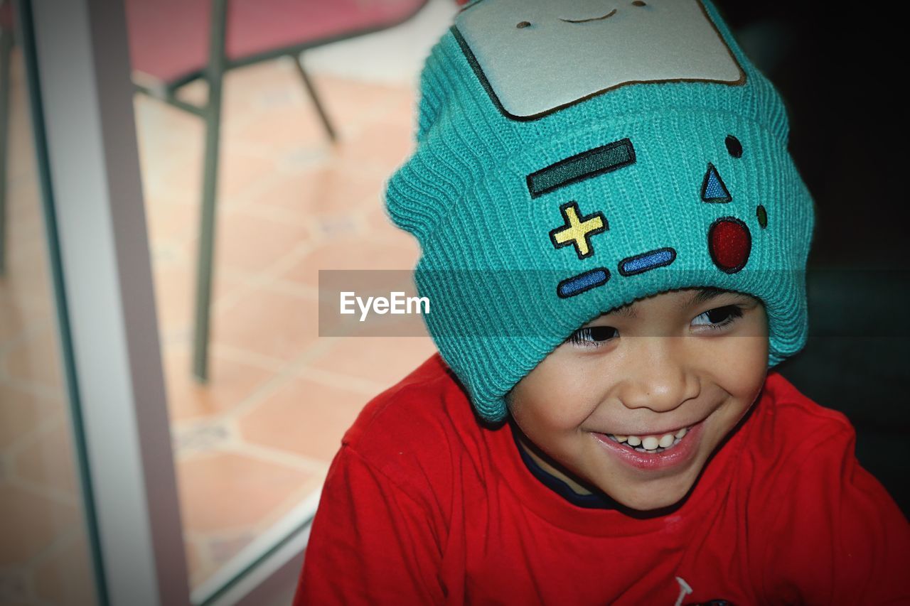 Close-up of cute cheerful boy wearing knit hat looking away at home