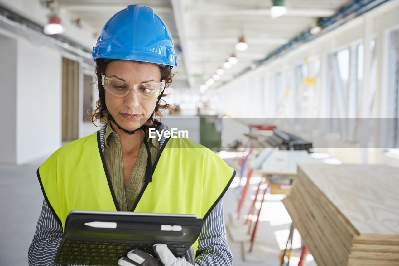 Confident female architect in reflective clothing using digital tablet at construction site