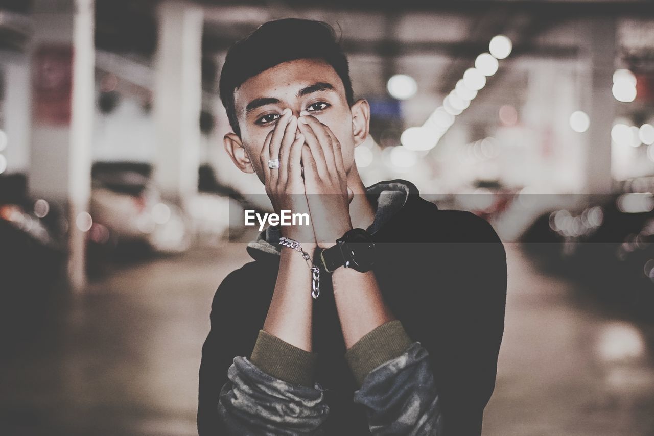 Portrait of shocked young man covering mouth while standing in parking lot