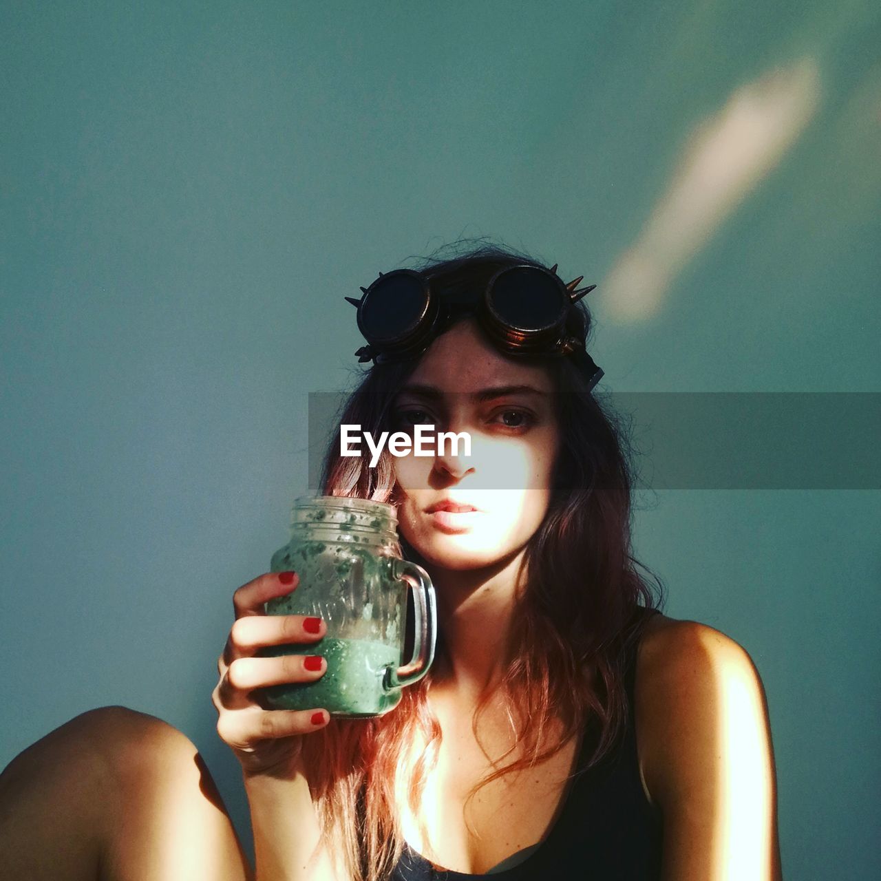 Portrait of young woman holding drink jar against wall