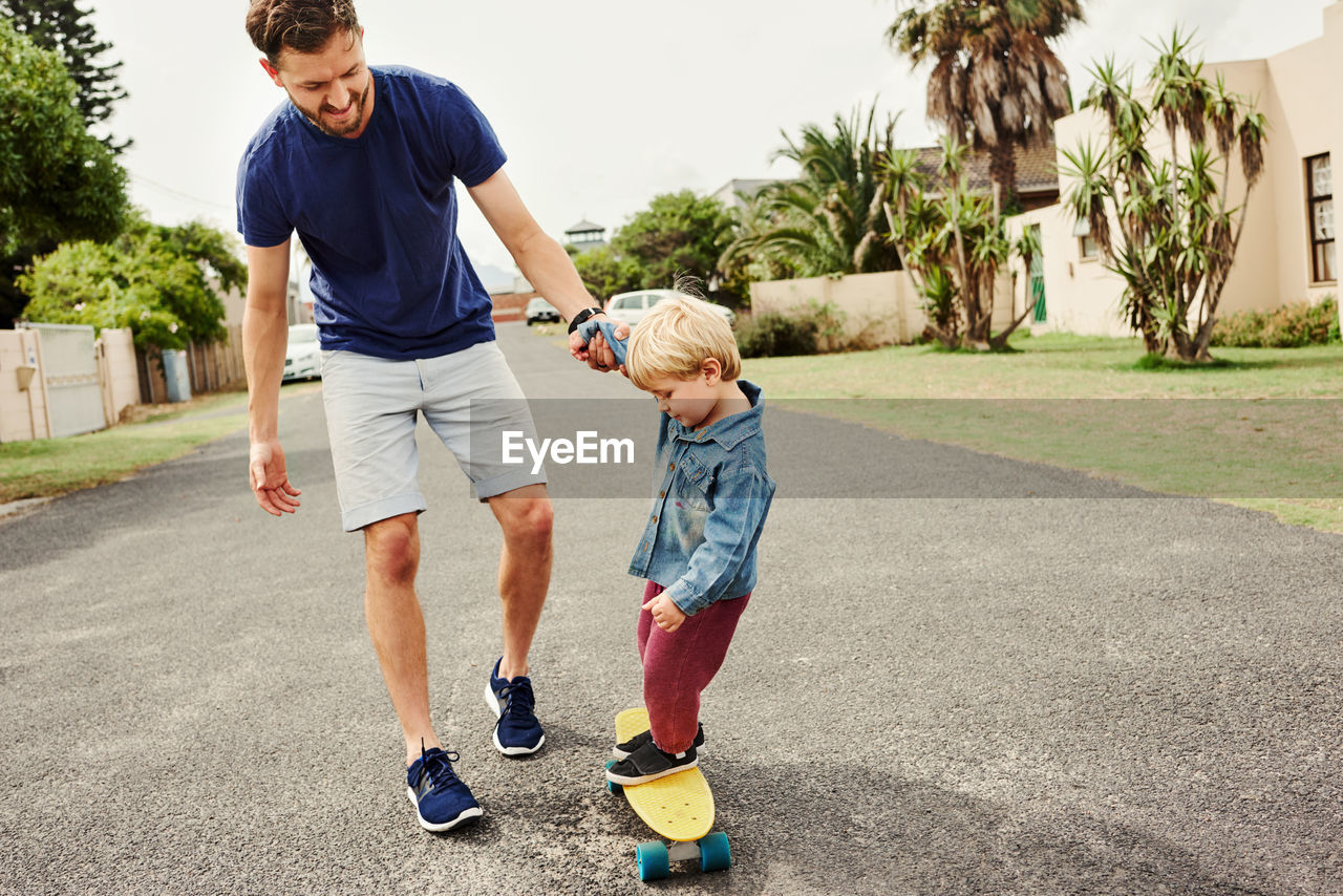 Father teaching skateboarding to son outdoors