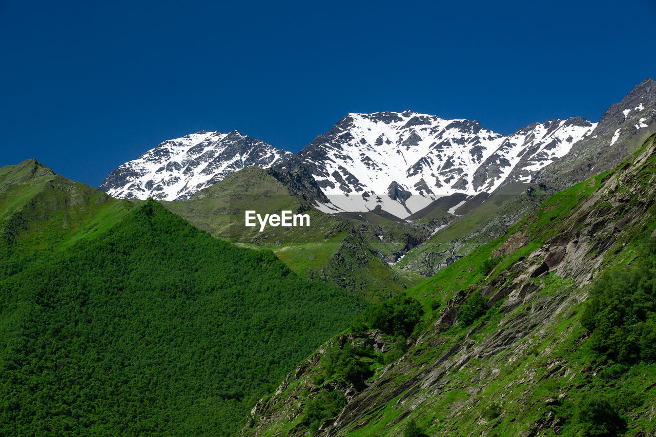 Beautiful green mountains covered with snow on the peaks