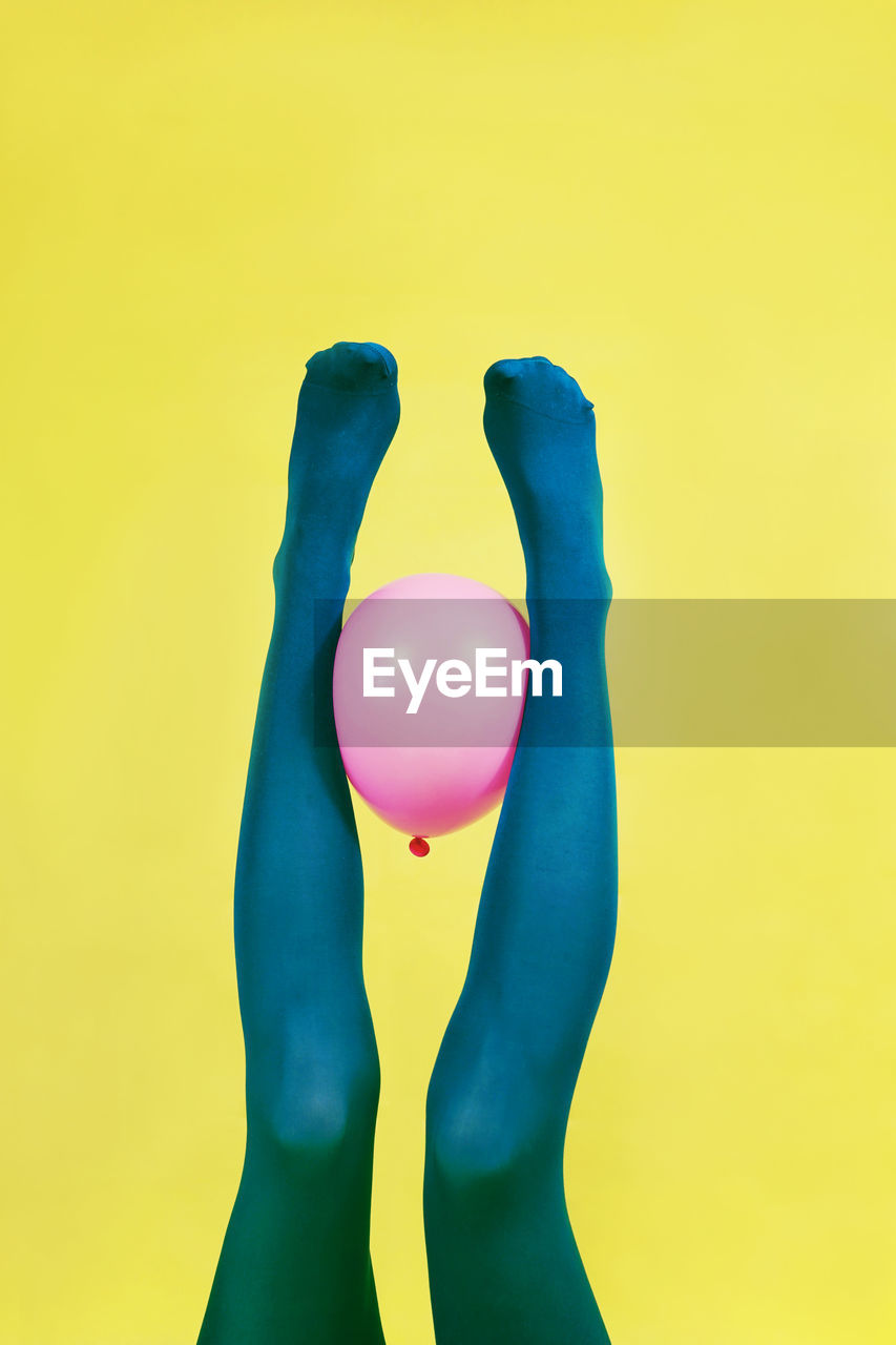 Low section of person holding pink balloon against yellow background