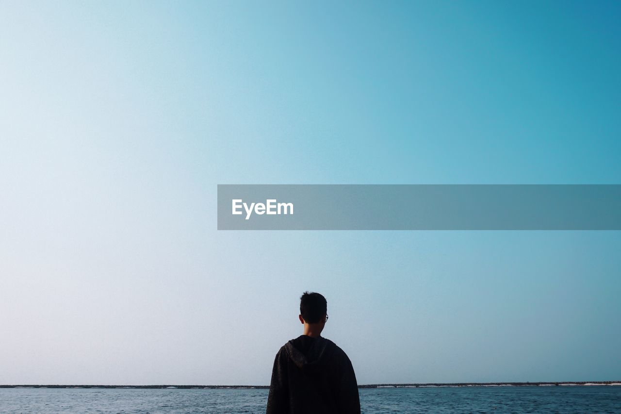 Rear view of man looking at sea against clear sky