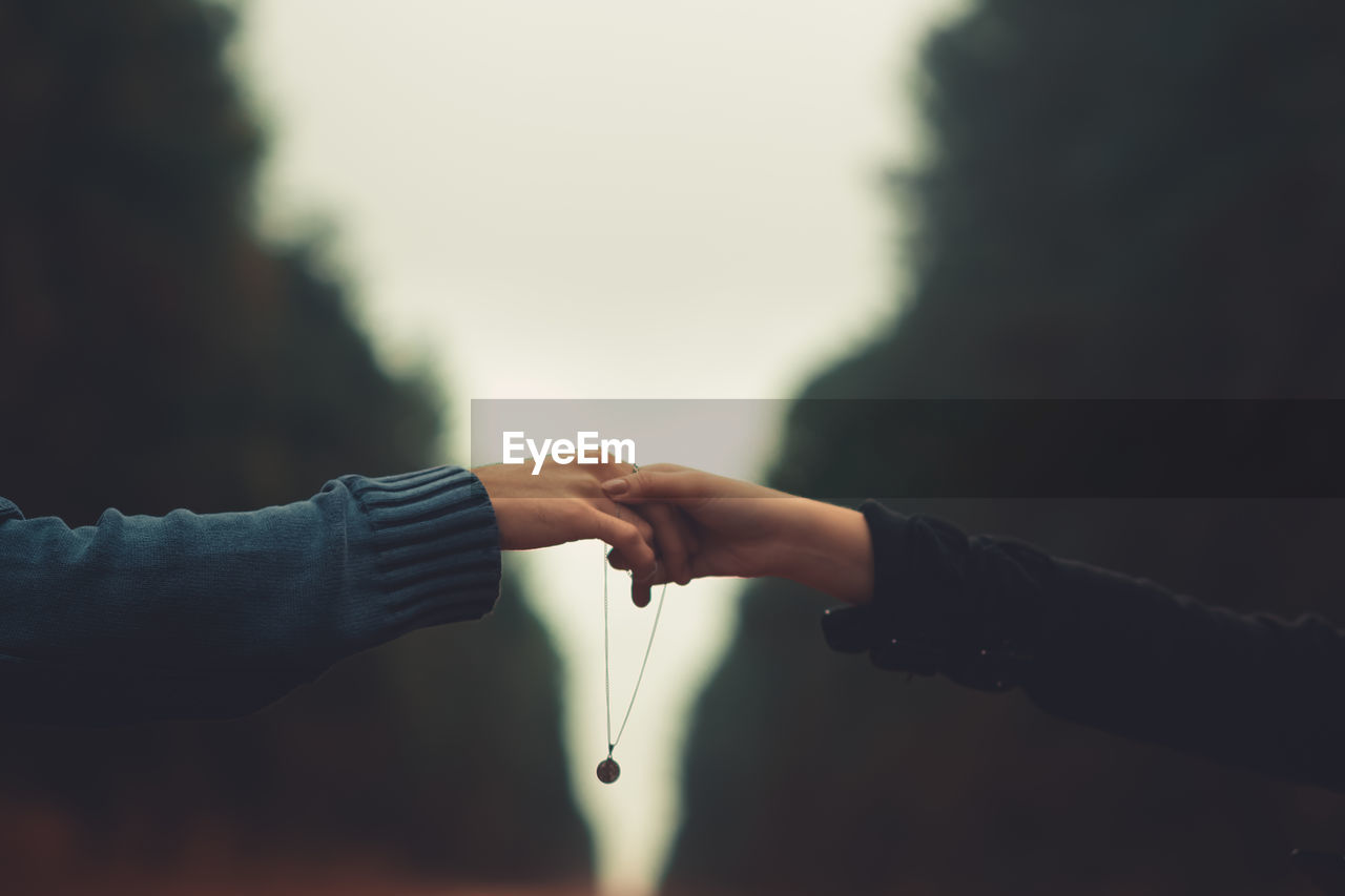 Cropped image of couple with necklace holding hands against sky