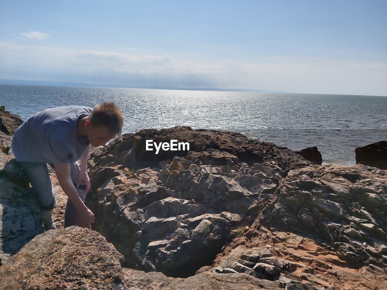 REAR VIEW OF BOY ON ROCK AT BEACH