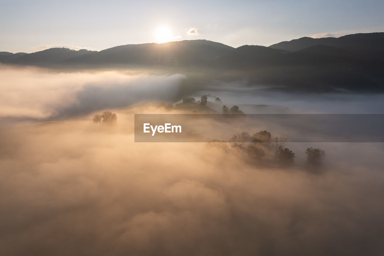 fog, environment, cloud, sky, mountain, mist, morning, landscape, scenics - nature, nature, beauty in nature, sun, dawn, land, sunlight, travel, sunrise, mountain range, sunbeam, horizon, mountain peak, no people, tranquility, outdoors, travel destinations, twilight, tourism, forest, idyllic, atmospheric mood, tree, tranquil scene, cloudscape, summer, social issues, plant, blue, silhouette, copy space