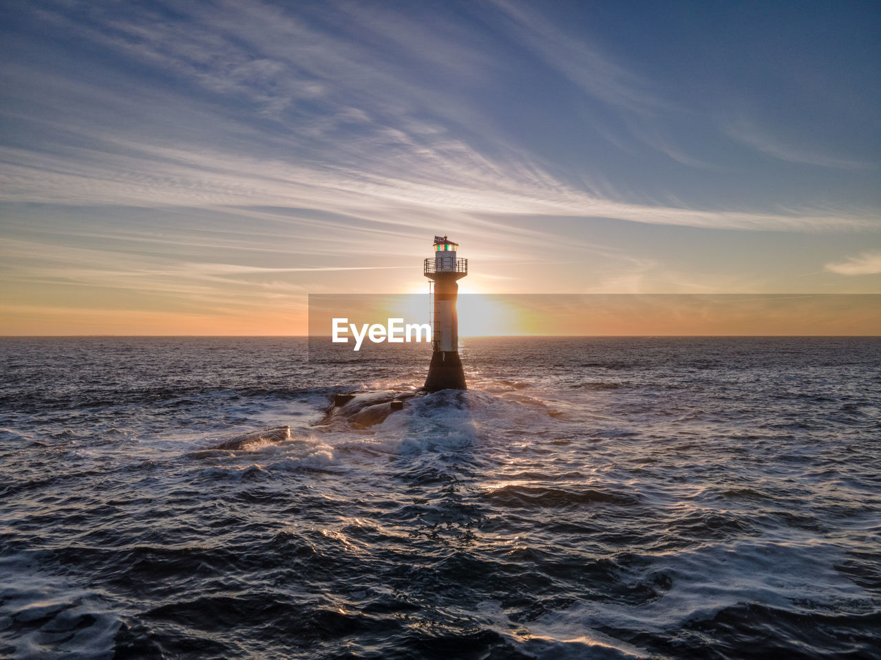 Lighthouse by sea against sky during sunset