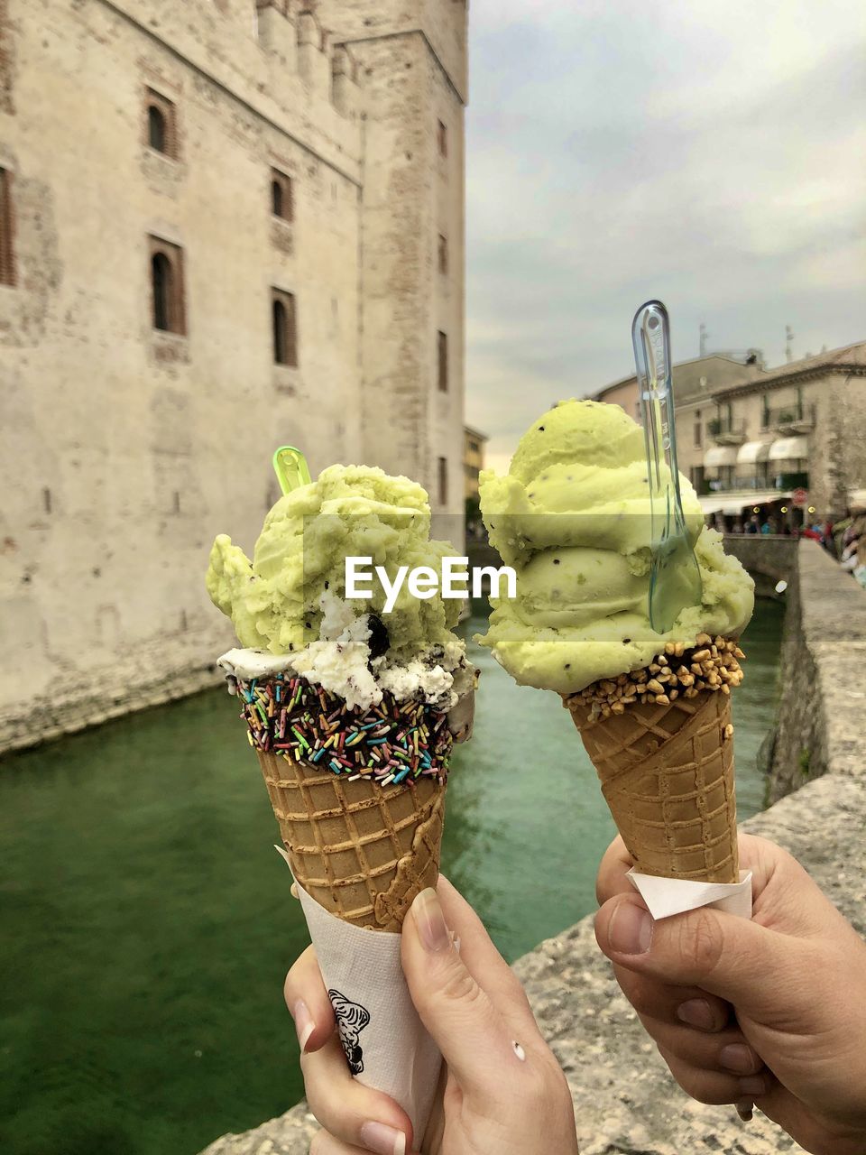 MIDSECTION OF PERSON HOLDING ICE CREAM CONE AGAINST WOODEN WALL