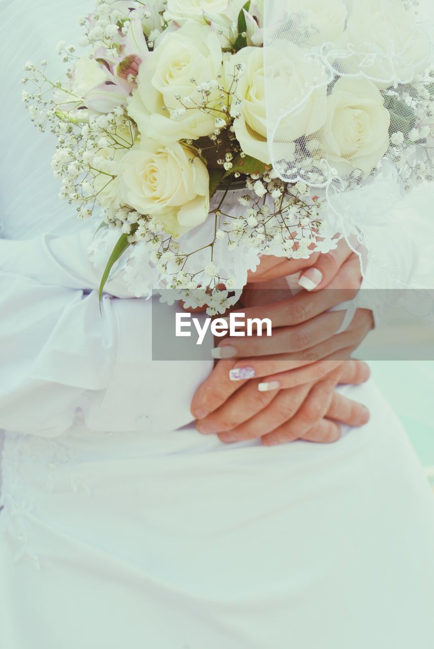 Cropped hands of bride and groom holding hands with bouquet