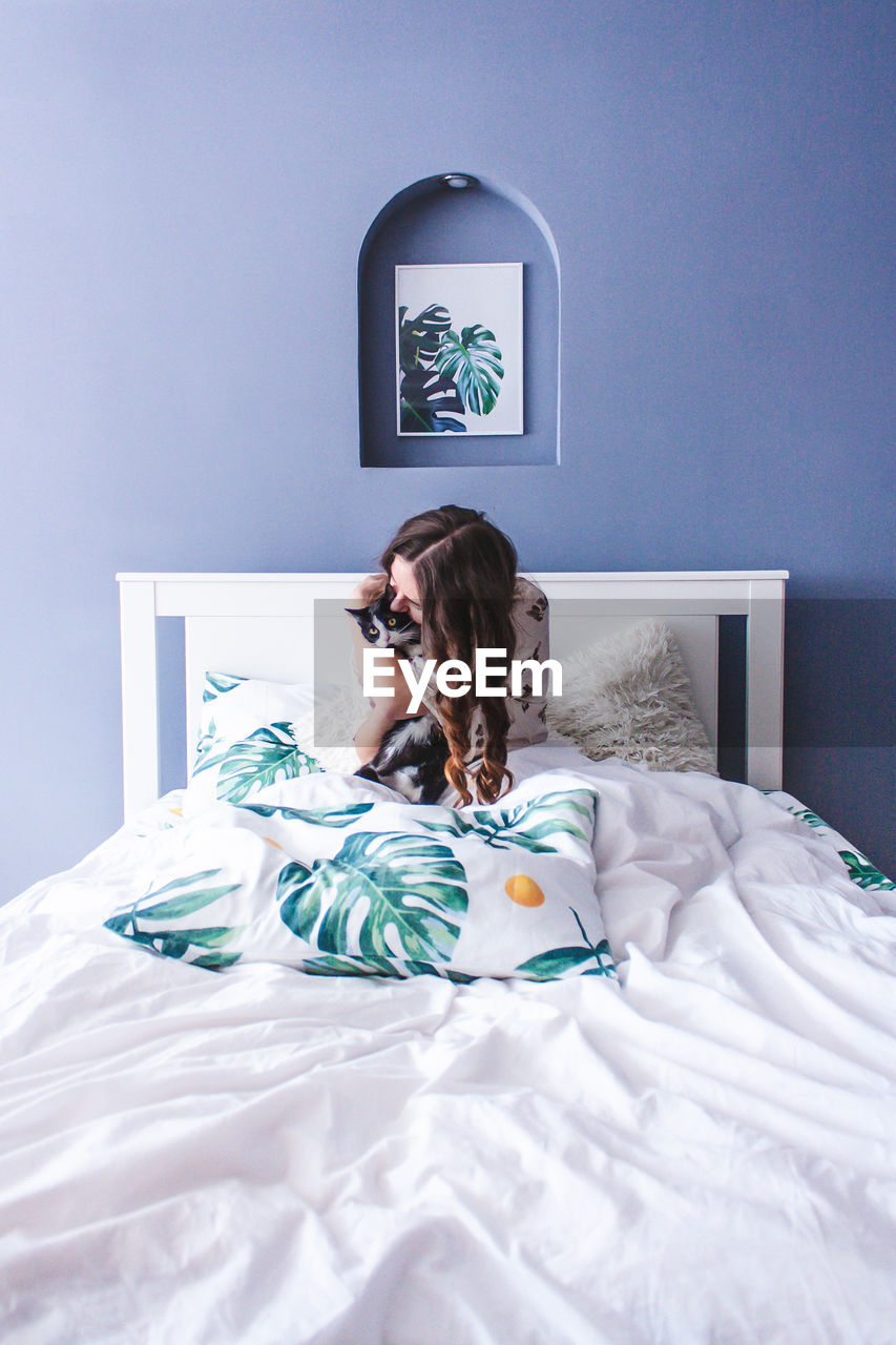 PORTRAIT OF WOMAN SITTING ON BED IN BEDROOM