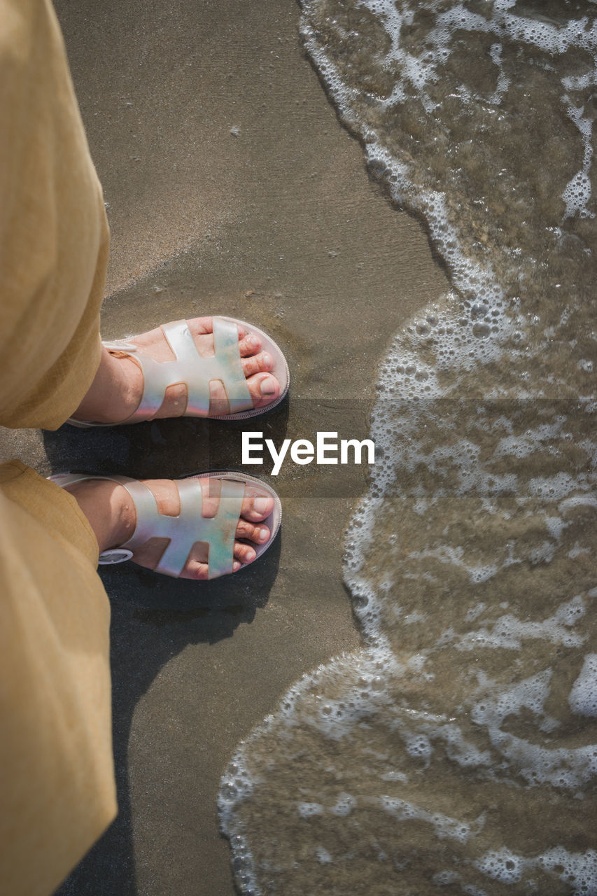 LOW SECTION OF WOMAN STANDING ON SANDY BEACH