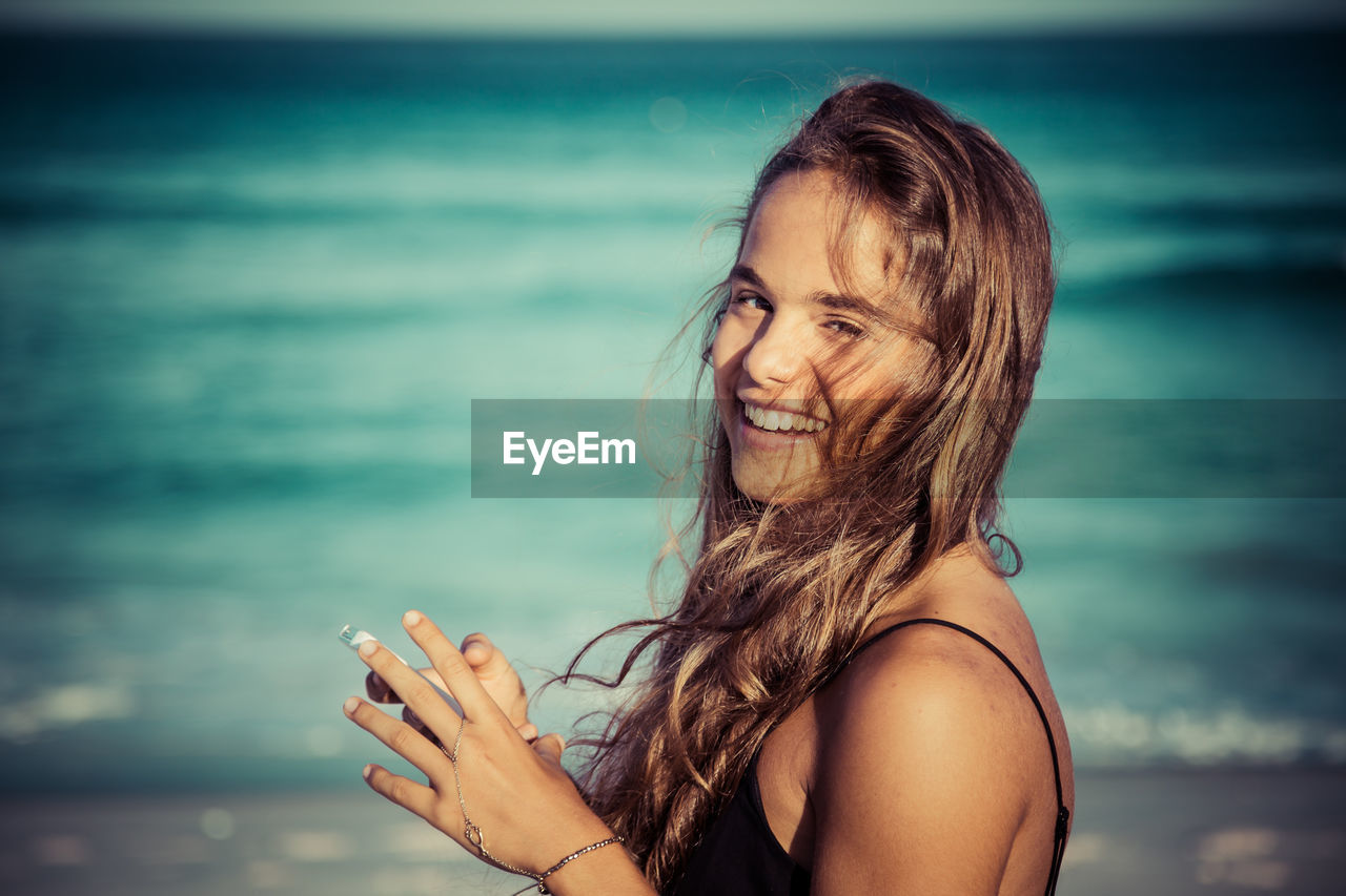 PORTRAIT OF SMILING WOMAN AGAINST SEA