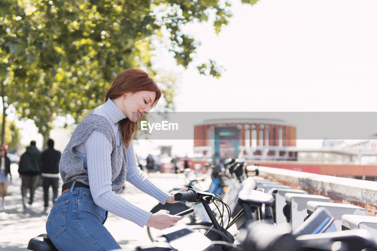 Smiling woman renting electric bicycle through smart phone app