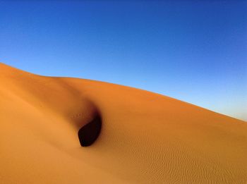 Sand dunes in desert against clear blue sky