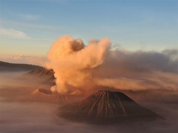 Smoke emitting from volcanic mountain against sky during sunset