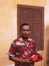 Portrait of man with telephone standing against window