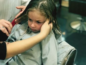 Cropped hand of hairdresser cutting girl hair in shop