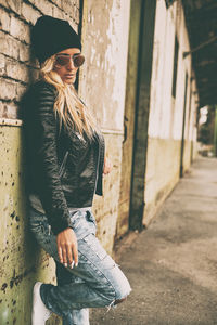 Fashionable young woman wearing jacket standing against brick wall