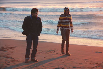 People standing on beach against sky during sunset