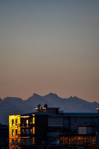 Silhouette buildings by mountains against clear sky at sunset