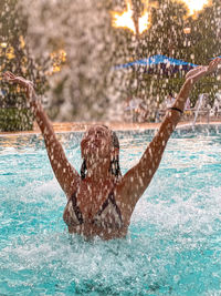 A young woman is enjoying staying under the waterfall in the swimming pool